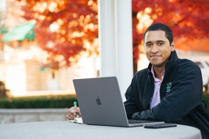 student on a laptop outside the library in the fall