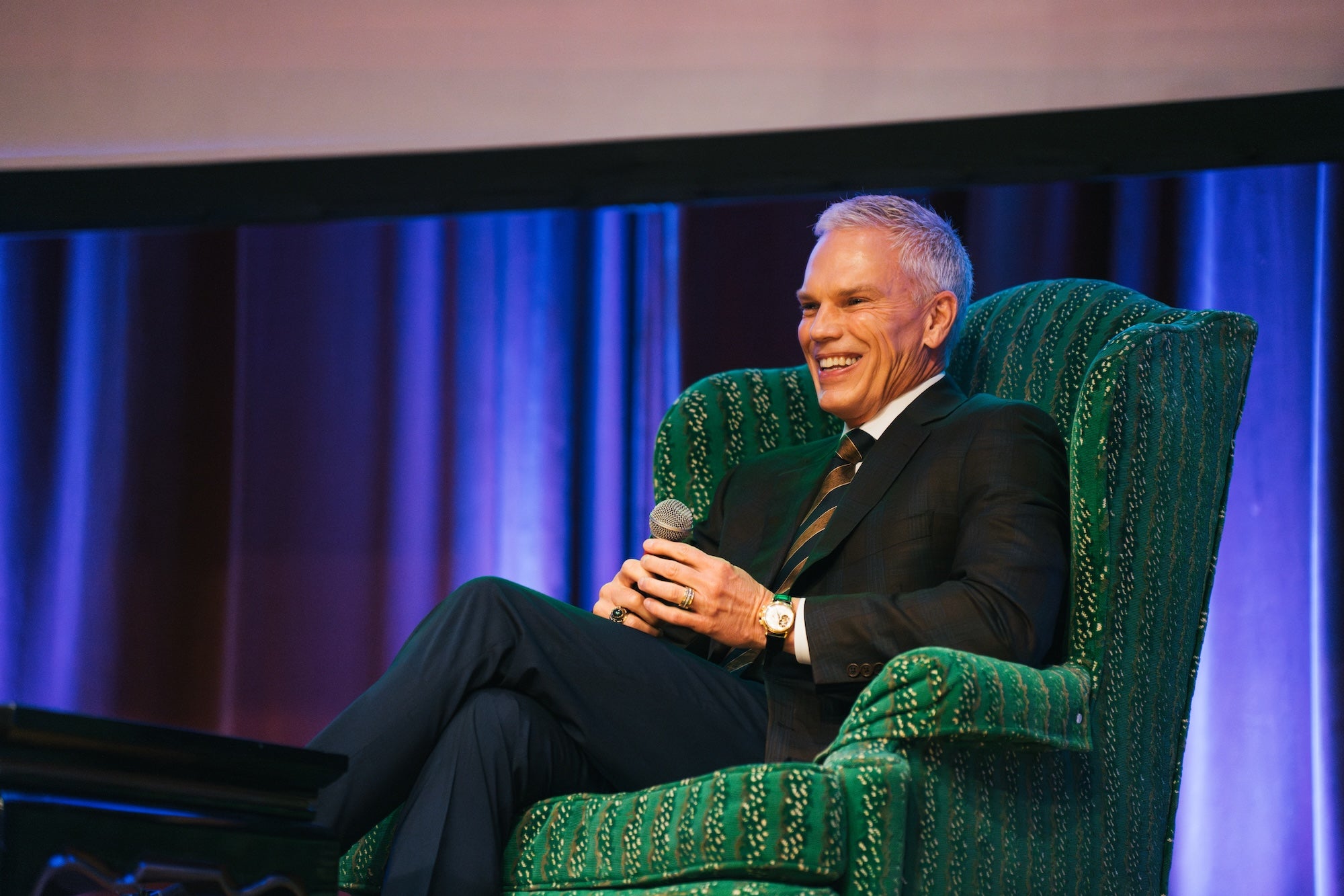 Brad D. Smith sitting in a green chair and holding a microphone