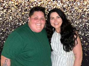 Mika Sheppard and Caylin France smile together for a photo in front of a silver, glitter background