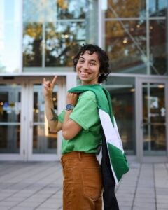 Michaela Marshall smiles with her graduation hood over her shoulder while standing in front of Marshall University's Drinko Library