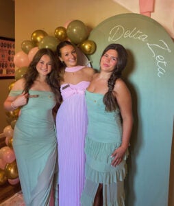 Three girls smile together at a sorority formal event
