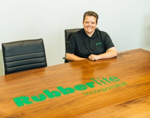 Alexie Adkins sits smiling at a Rubberlite Inc. conference table