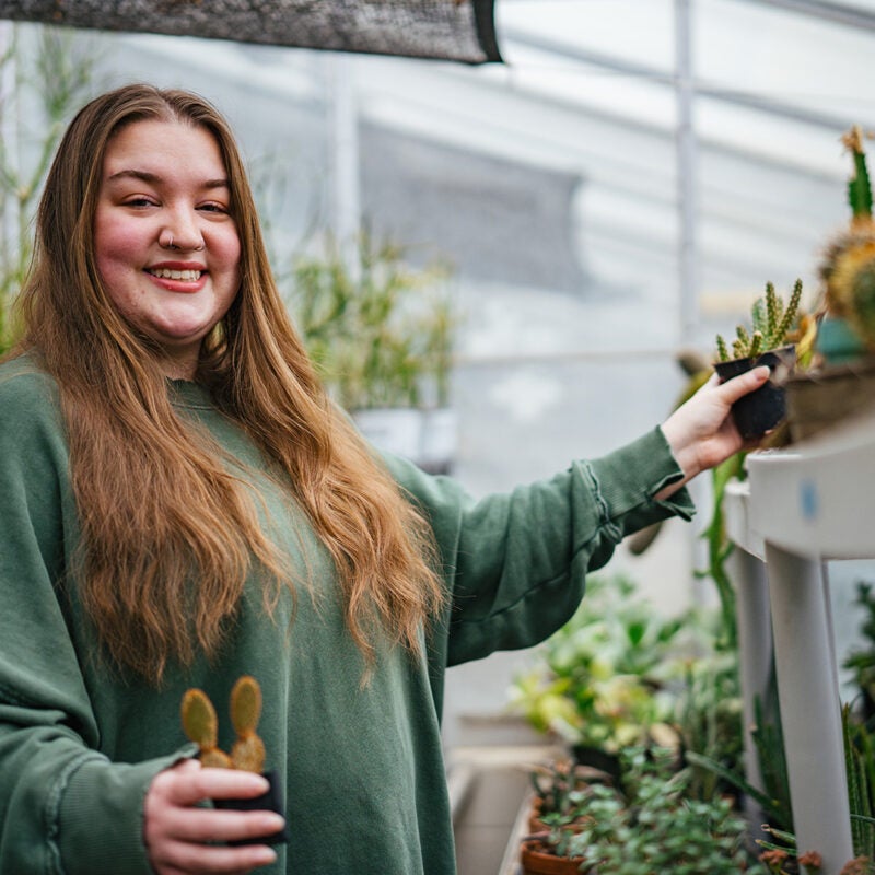 A student smiles while working with plants in the Marshall University greenhouse
