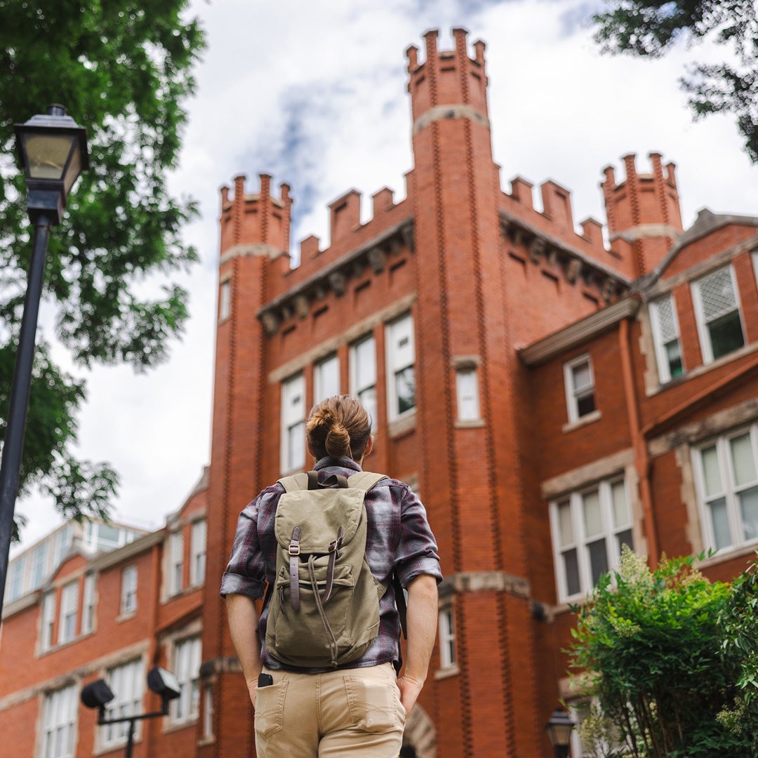 A student wearing a backpack looks up at Marshall University's Old Main