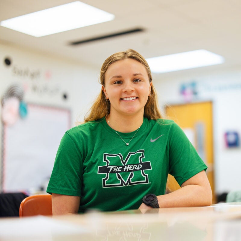 A student teacher sits in a classroom wearing a Marshall University shirt