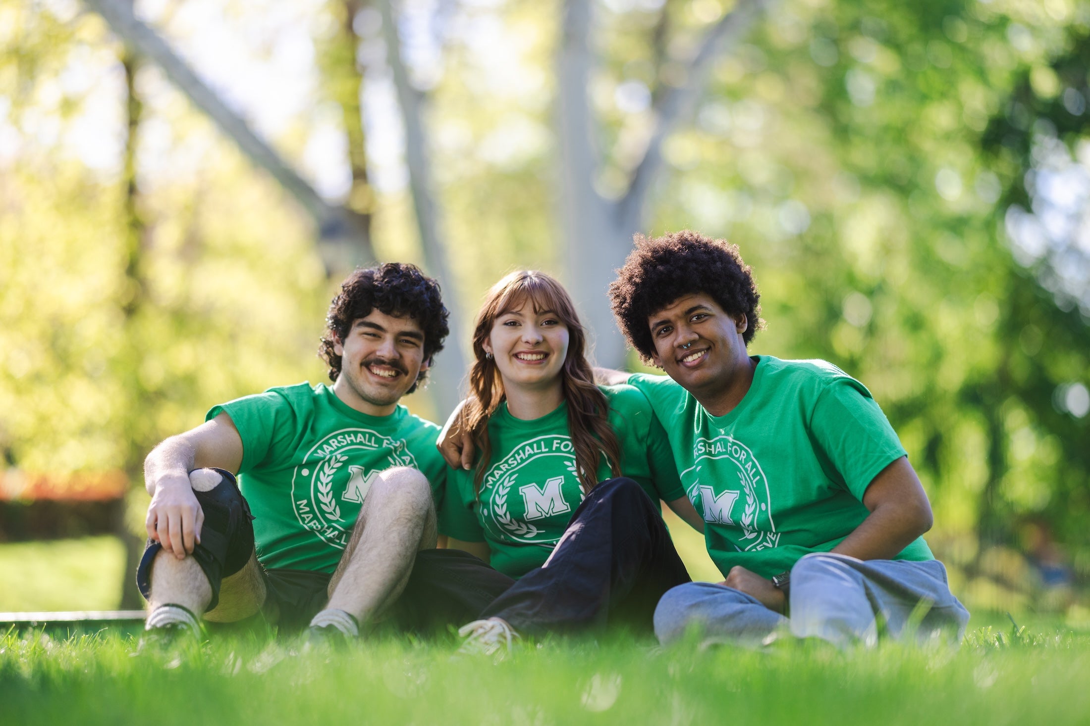 three students smiling at the camera sitting on the ground