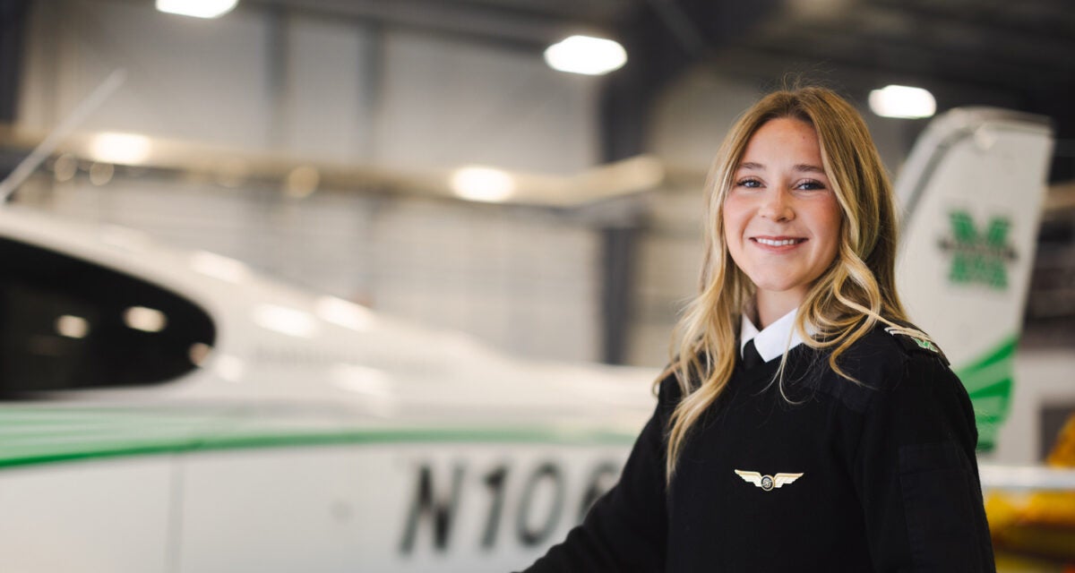 Marshall University Aviation student stands in front of plane while wearing a pilot uniform