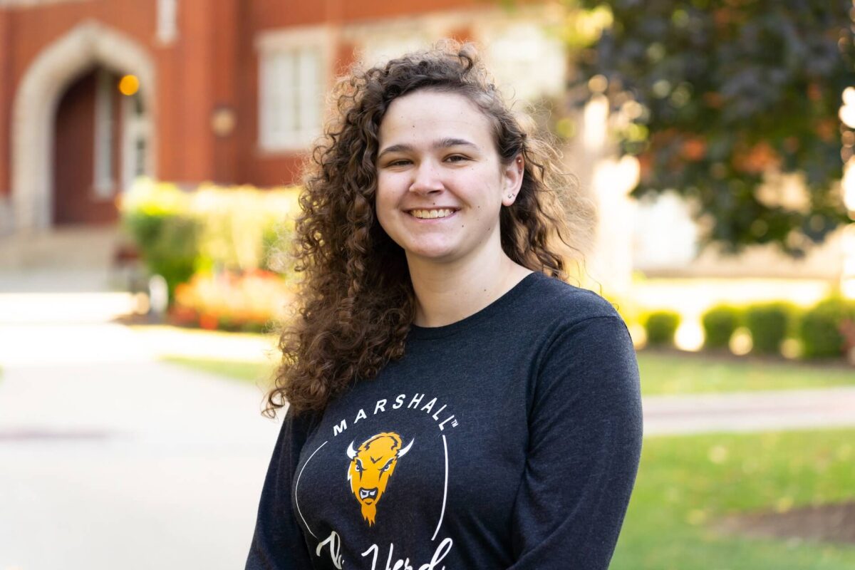 student in front of Old Main smiling at the camera