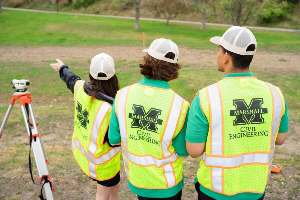 three students in reflective vests practicing surveying