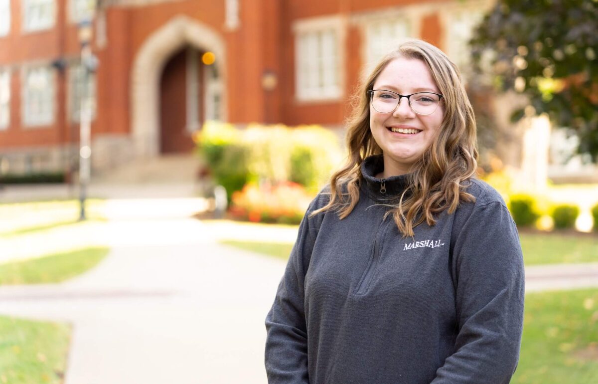 student outside Old Main smiling at the camera