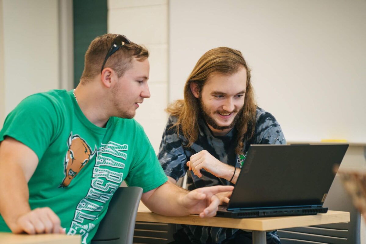 two students working on a laptop together in a classroom