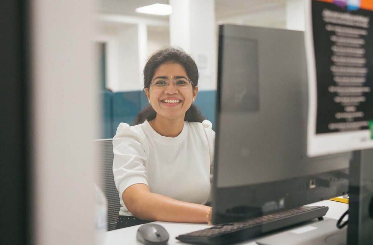student on a desktop computer through a window, smiling at the camera