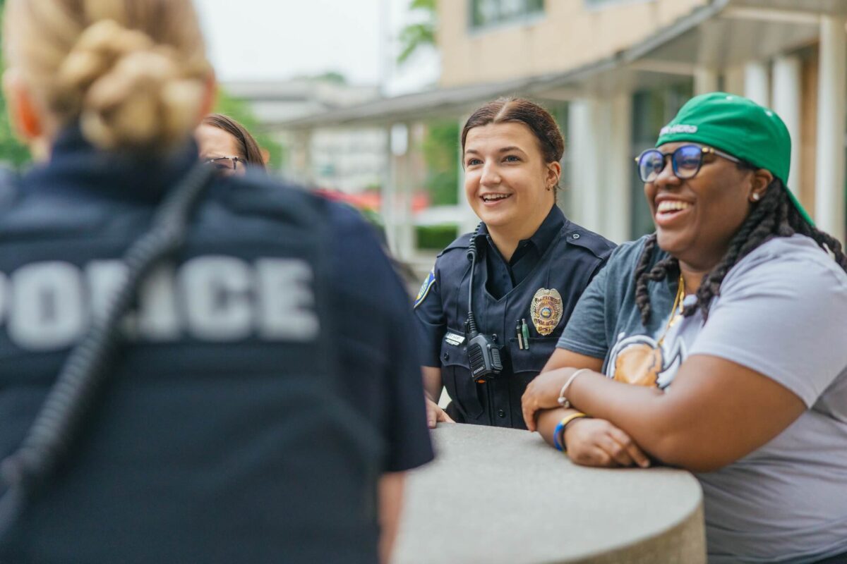 two police officers talking to a student and smiling outside on campus