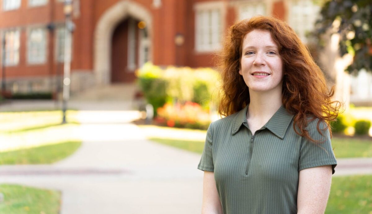 student outside Old Main and smiling at the camera