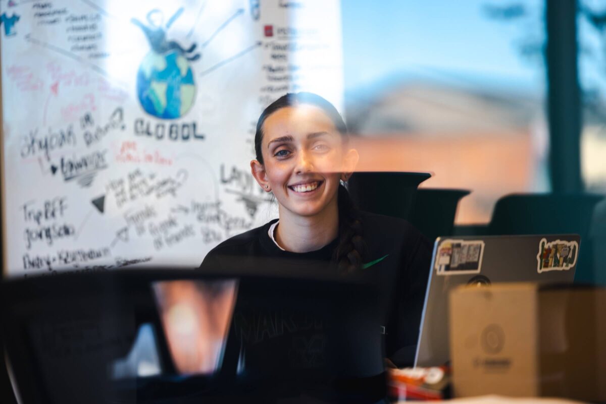 student smiling at a camera through a window