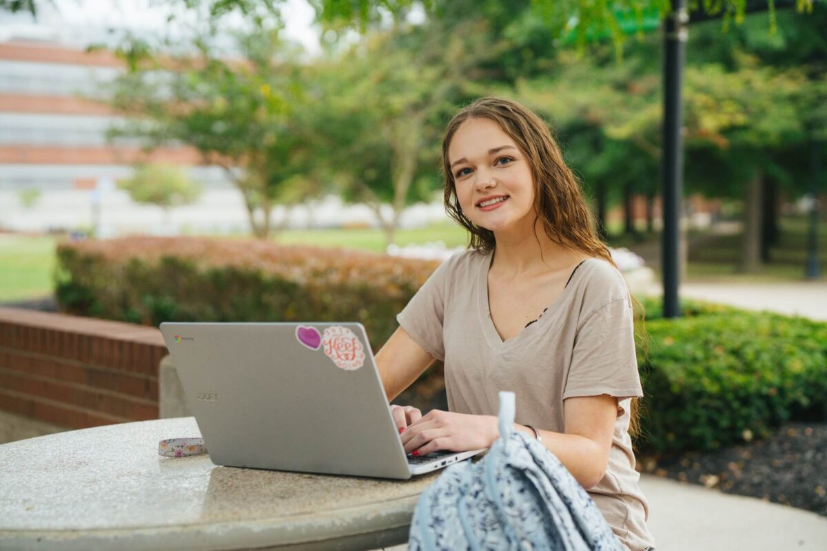 student working on a laptop at a table outside the Memorial Student Center