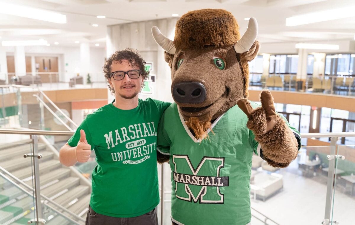 student smiling with Marco inside the Memorial Student Center, both showing a Go Herd symbol with their hands