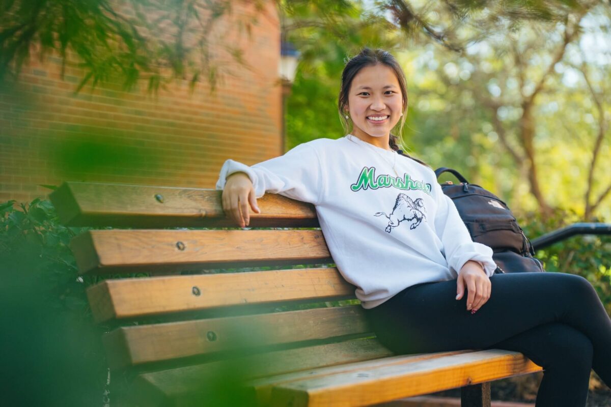 student sitting on a bench outside on campus and smiling at the camera