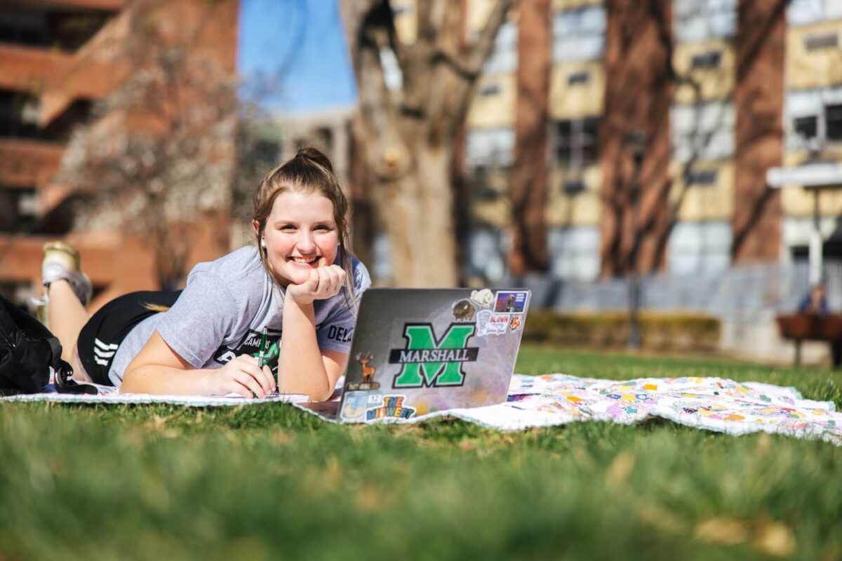 student studying on a laptop laying on a blanket on Buskirk field