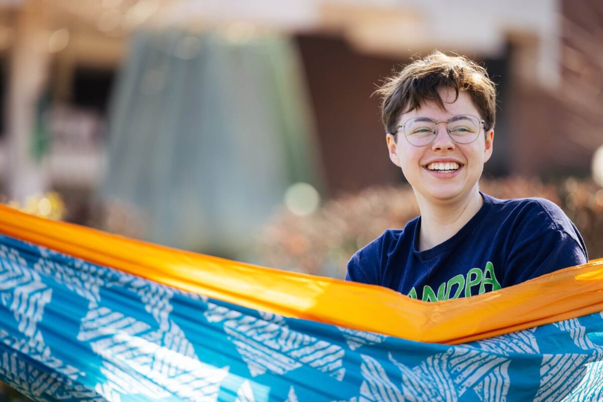 student sitting in a hammock outside on campus in front of the Memorial Fountain
