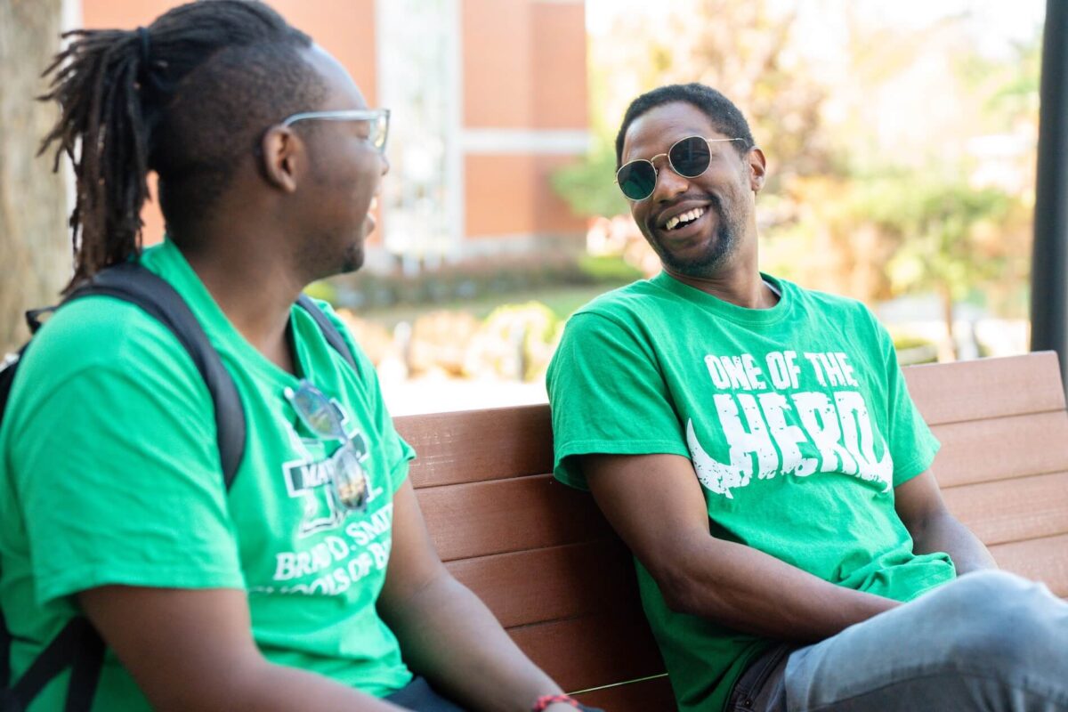 two students laughing and talking on a bench outside of Old Main