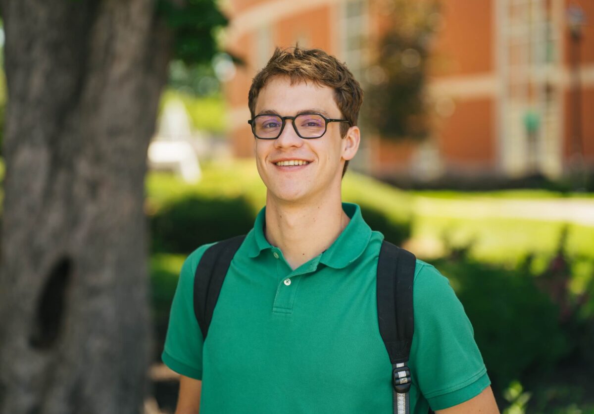 student outside of Old Main with a backpack on smiling at the camera