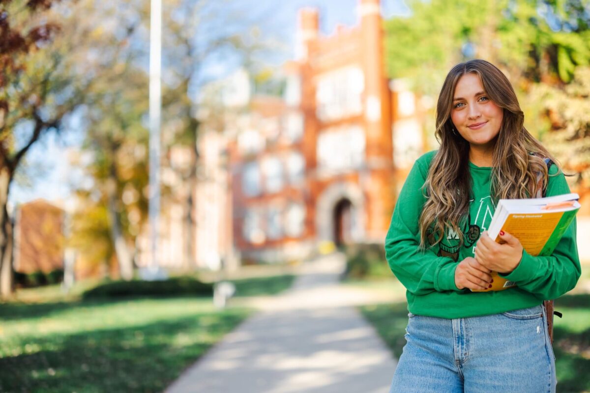 student holding books smiling at the camera outside Old Main