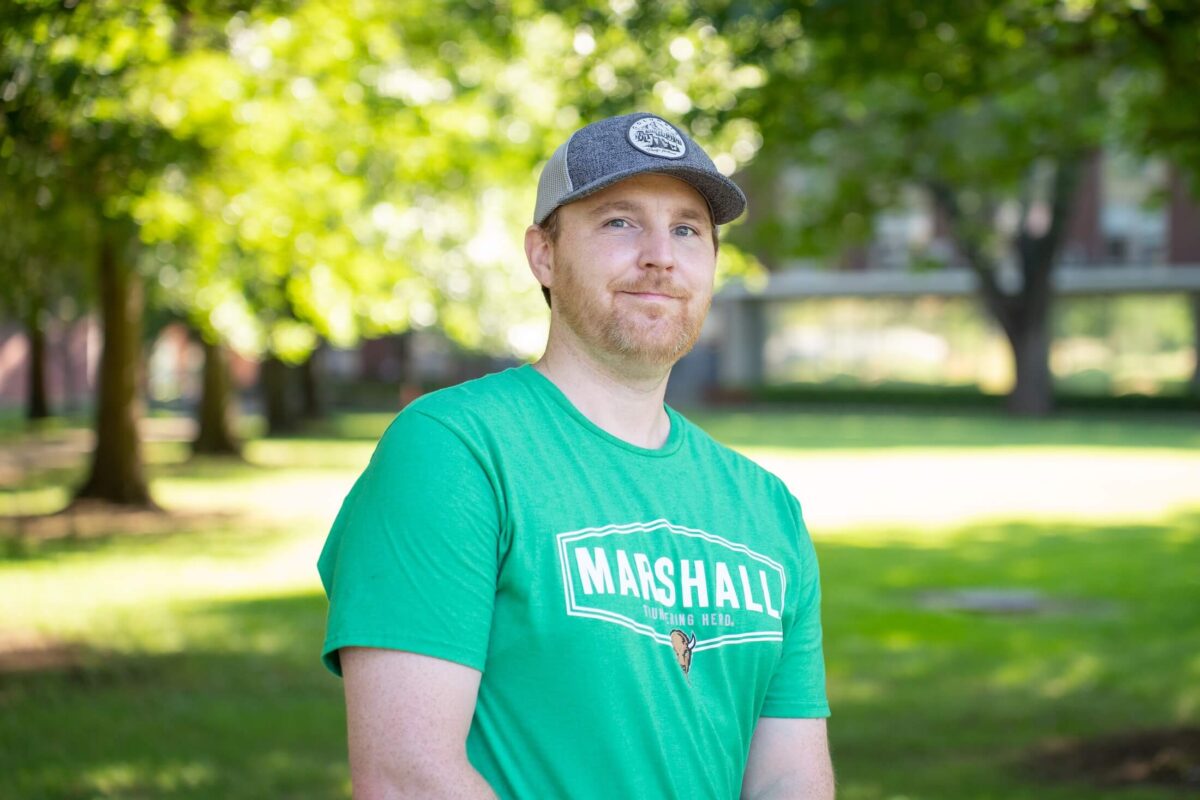 student in a hat smiling at the camera outside on campus