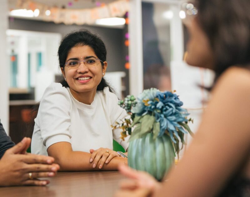 student talking to two other students inside at a table
