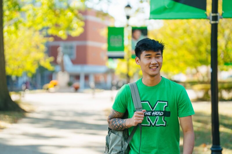 student walking across campus with a Marshall t-shirt on