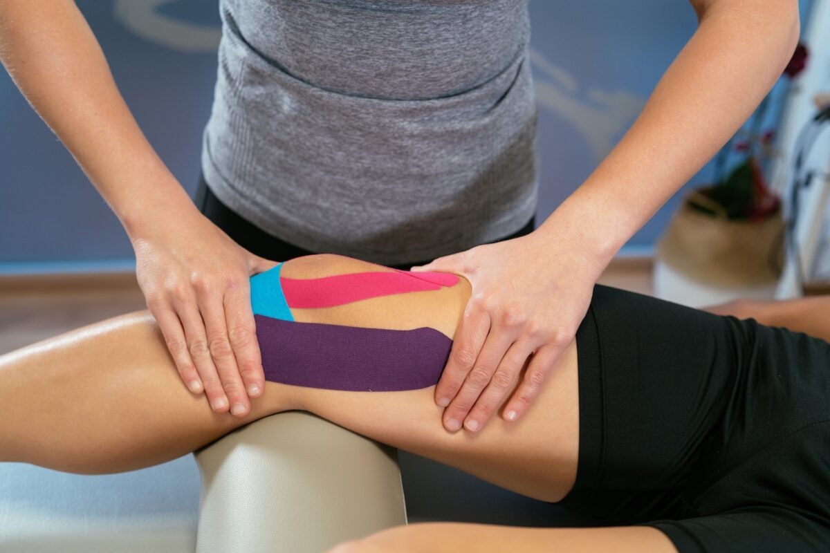 The hands of a woman physiotherapist pressing on a patient's knee with three medical tapes, purple, light blue and pink. Concept of muscle health and relaxation. Close-up