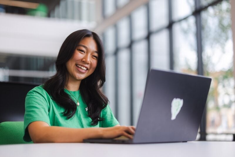 student working on a laptop and smiling in the business school