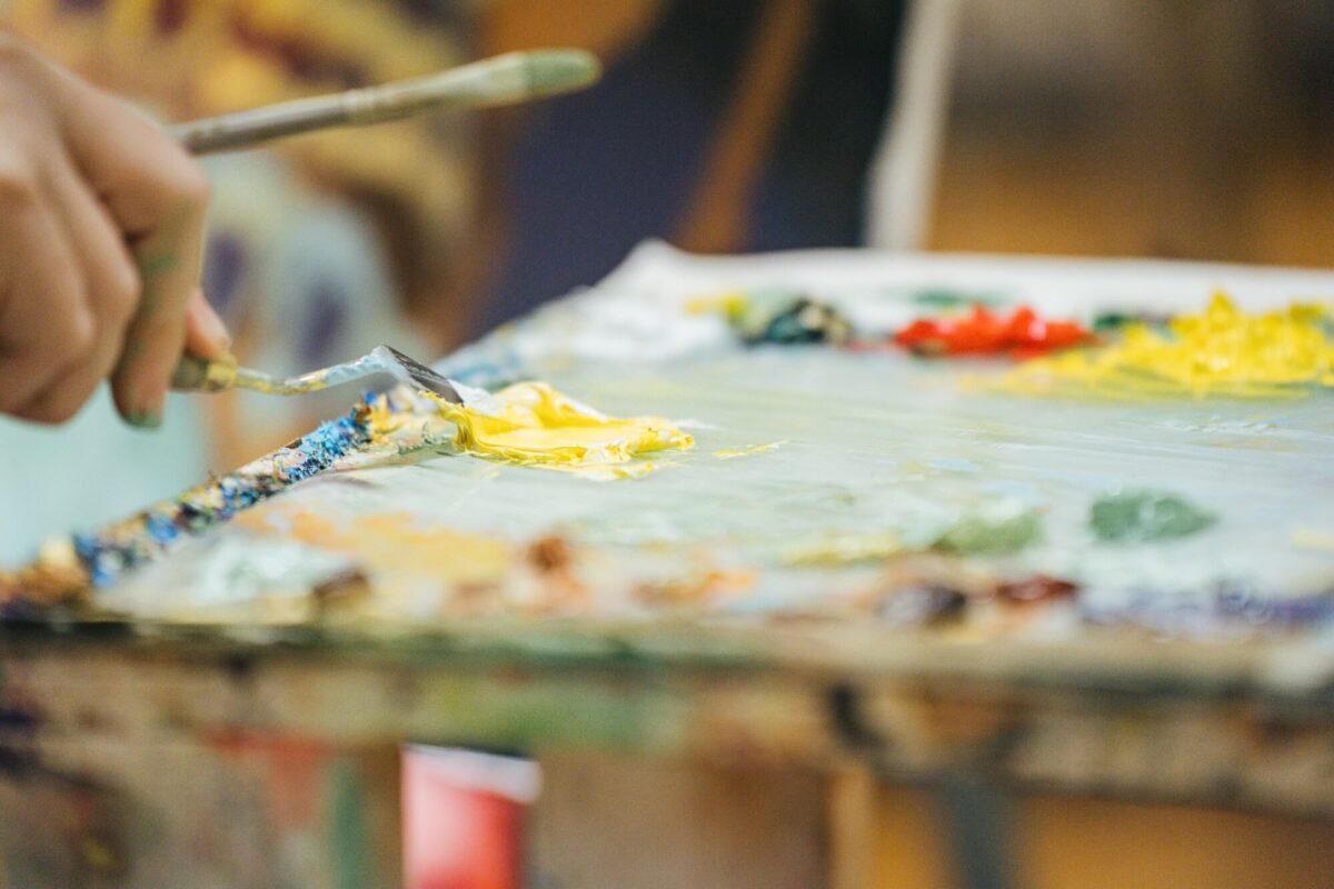 Close-up of an artist mixing paint colors on a palette with brushes and painting tools nearby.