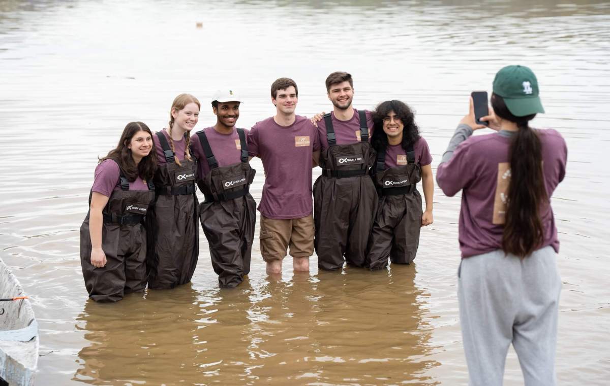 six students wading in a river smiling at another student taking a photo
