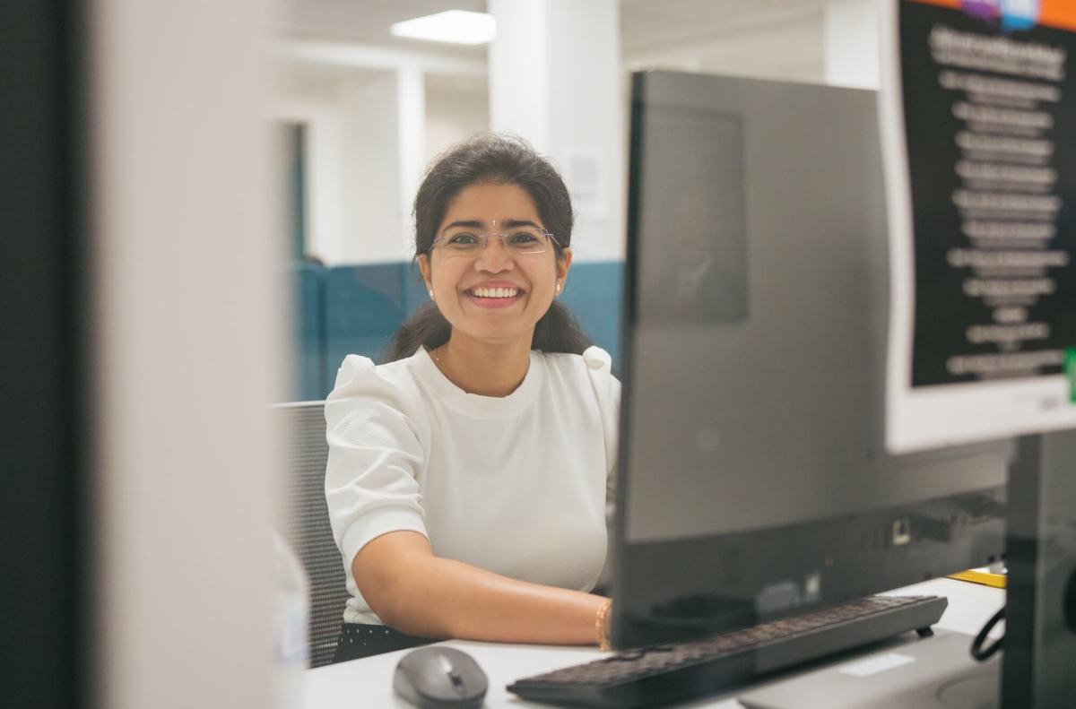 student on a desktop computer through a window, smiling at the camera