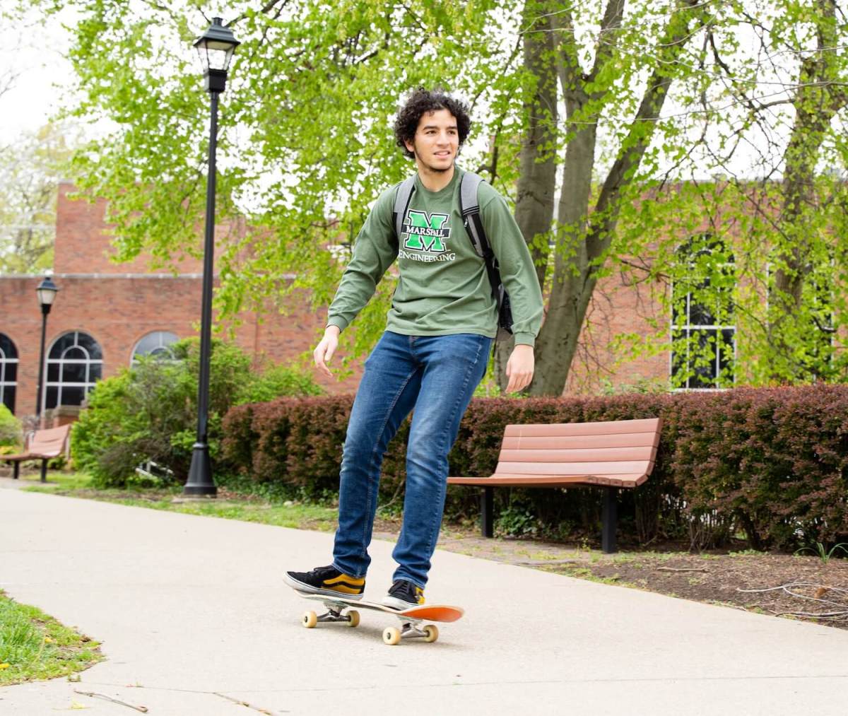 student riding a skateboard through campus in an engineering sweatshirt