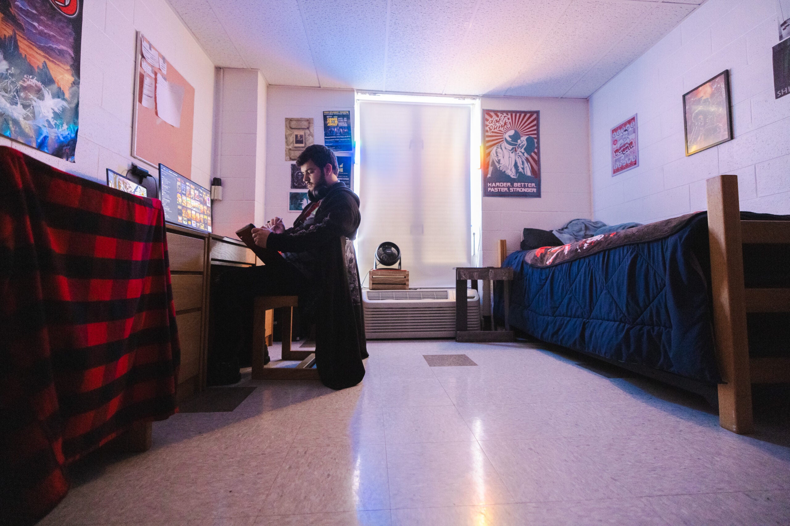 A students wears headphones while working on a computer in a college dorm room