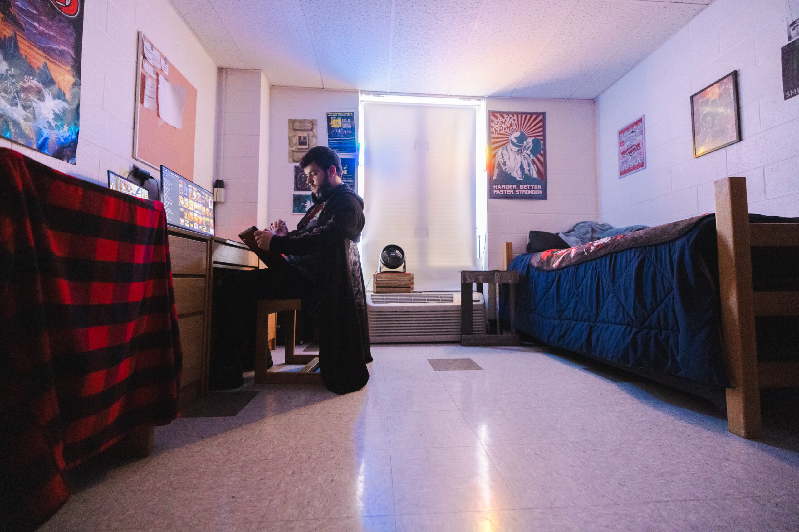 A students wears headphones while working on a computer in a college dorm room