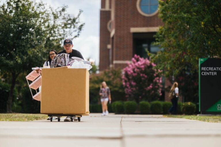 students pushing rolling moving bins in across campus