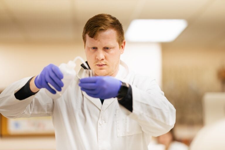 student working in a lab in a lab coat using test tube type materials