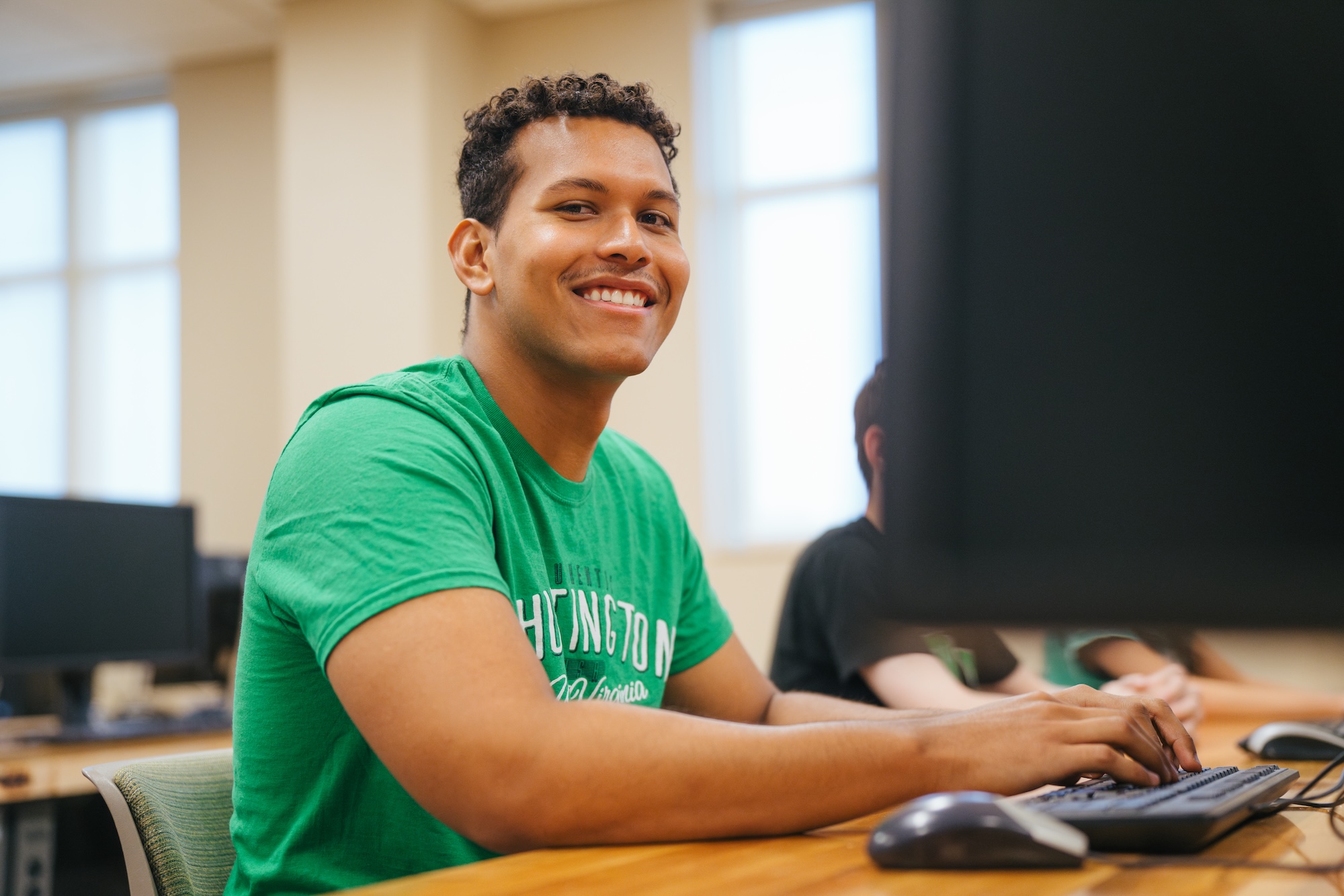 student working on a desktop computer and smiling at the camera