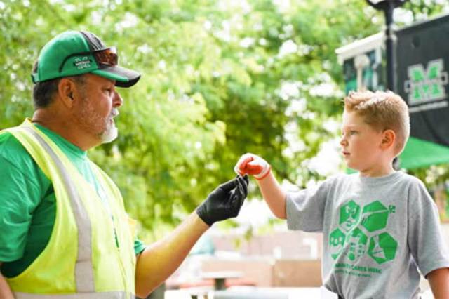 Facilities worker and young volunteer participate in a campus beautification activity beneath mature trees.