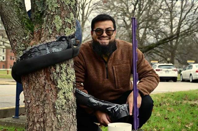 Graduate student installs research equipment on a campus tree to measure how rainfall is intercepted and dispersed by the tree canopy. Collection devices and measuring instruments are positioned around the trunk and beneath the tree.