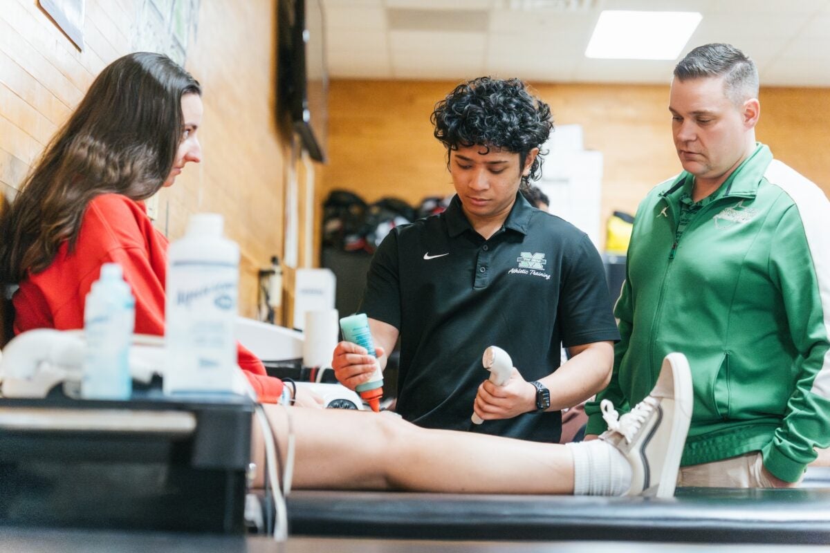Student Athletic Trainer giving another student a knee ultrasound with a professor supervising