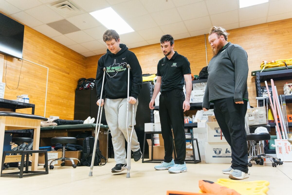 students helping a person on crutches learn to walk with a professor supervising