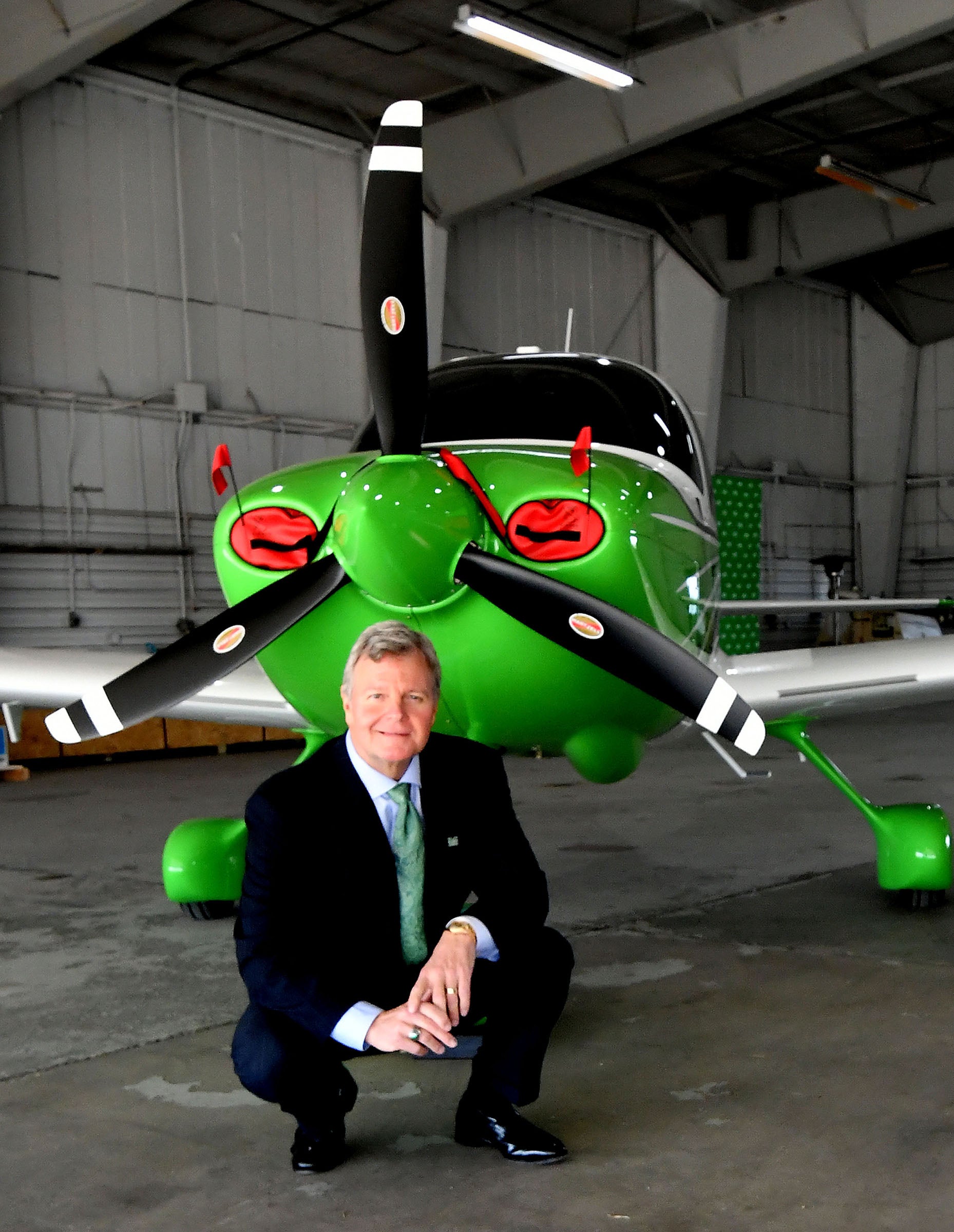 Bill Noe squats in front of a Marshall University branded plane