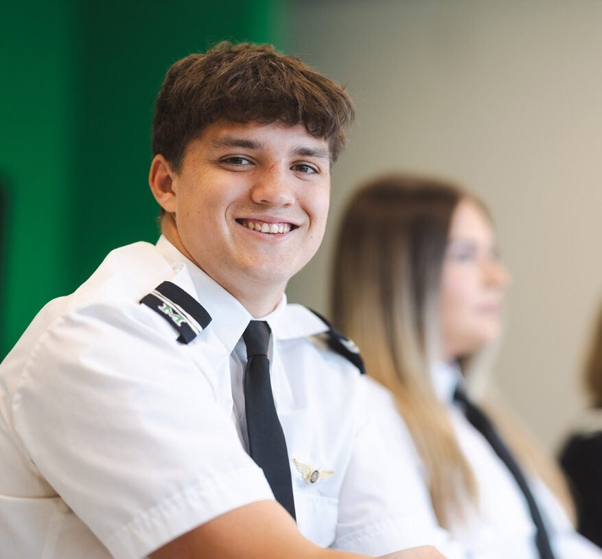 Aviation student smiles at the camera while sitting in class wearing a flight uniform