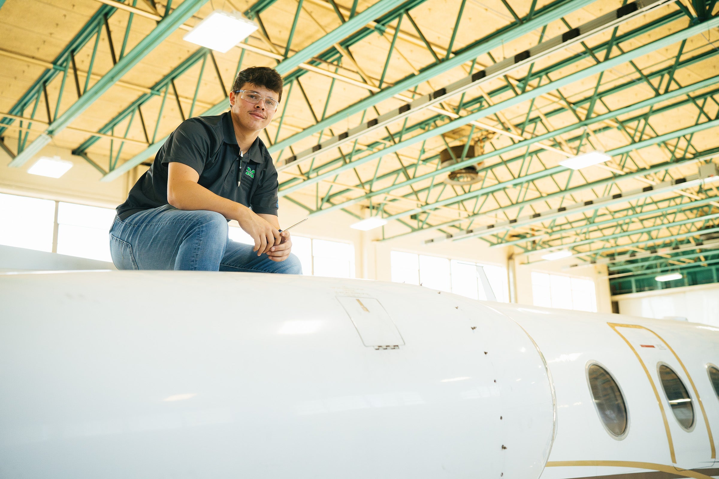 Marshall University Aviation Maintenance Technology student sits on the top of an aircraft while looking at the camera.