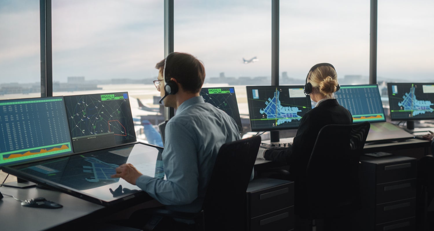 Aircraft Dispatcher work on computers while overlooking the runway from an airport tower.
