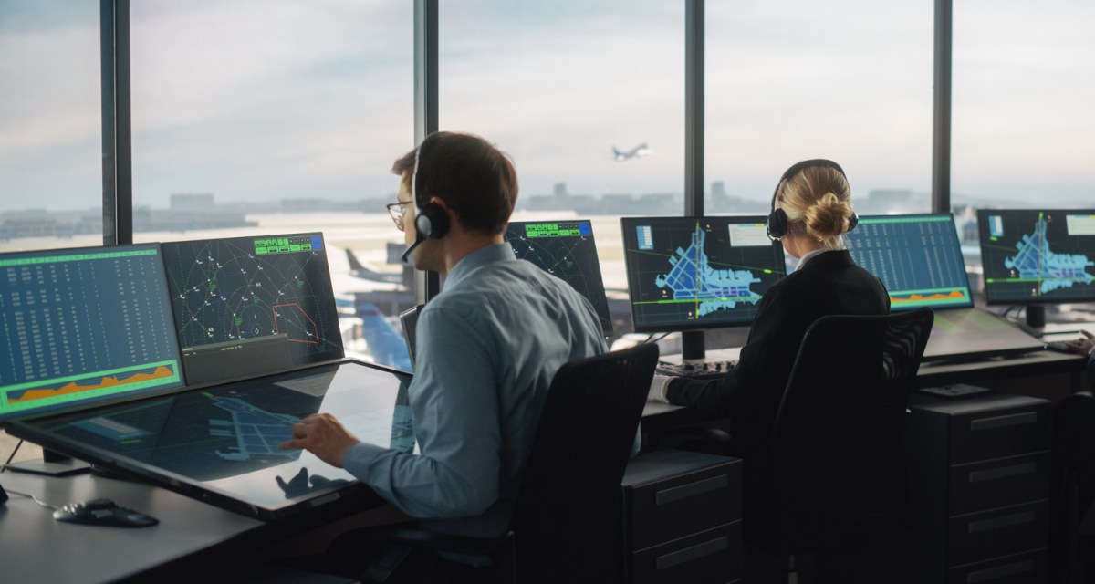 Aircraft Dispatcher work on computers while overlooking the runway from an airport tower.